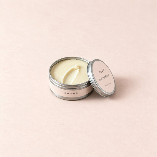 En öppen aluminiumburk med Raw Shea Butter från SAVÁS, locket lutat mot burken, på rosa bakgrund